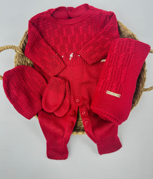 Conjunto Saída Maternidade Vera em tricô vermelho com macacão, manta, gorro e luvas, dispostos sobre cesta de palha